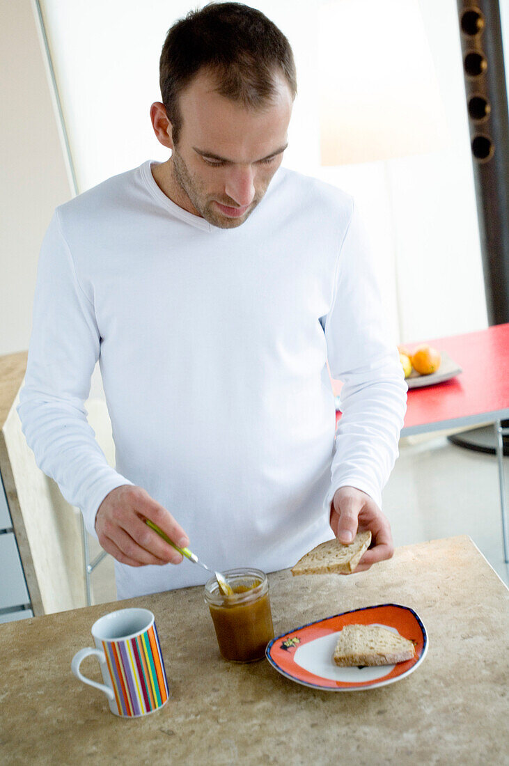 Man standing in the kitchen, spreading slice of bread with jam