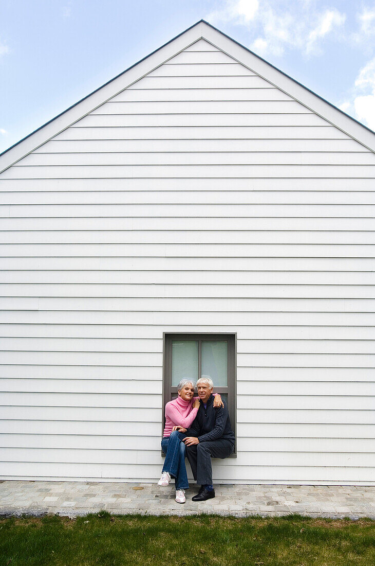 Senior couple embracing, sitting on a window sill
