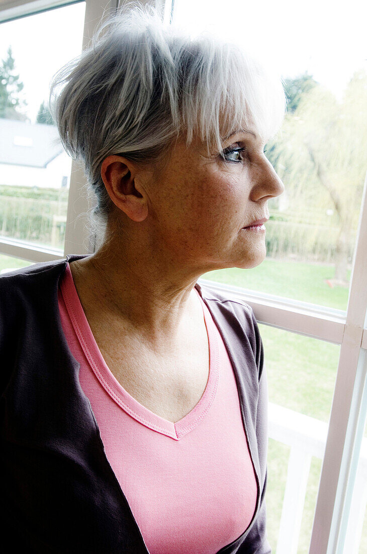 Thinking senior woman looking through a window