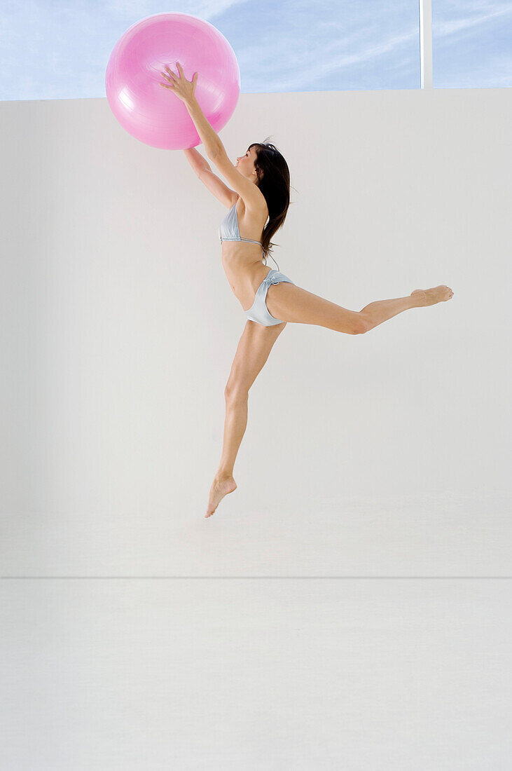 Young woman in bikini, jumping, holding big pink balloon