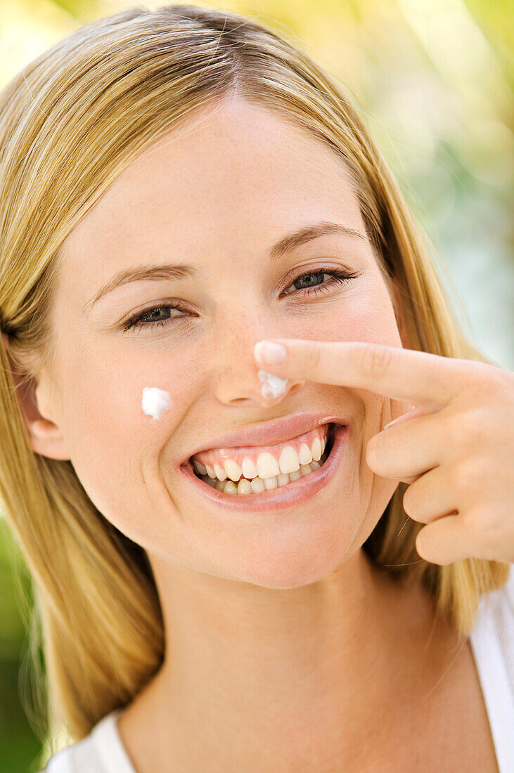 Portrait of a young woman applying moisturizer on her face, outdoors