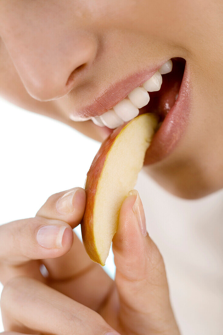 Portrait of a young woman eating a piece of apple, indoors