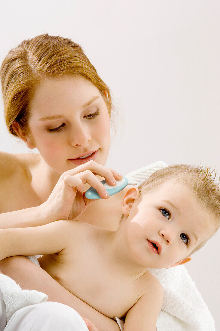 Close-up of a young woman combing hair of her son and smiling