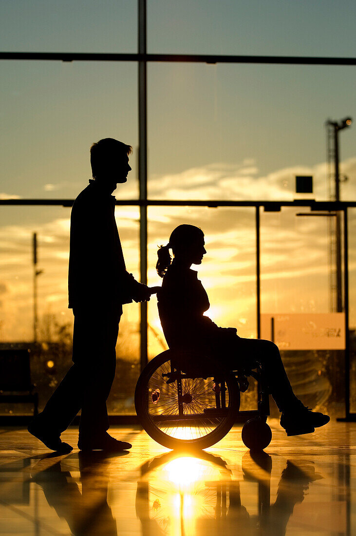 Silhouette of a man pushing a female patient sitting in a wheelchair