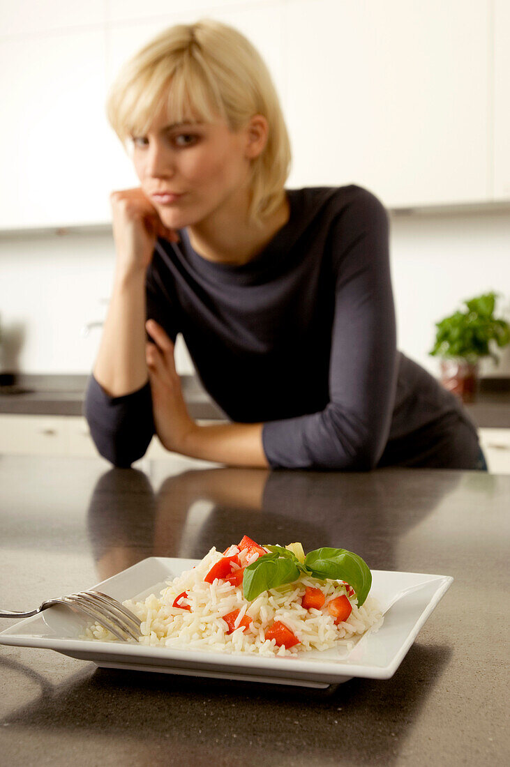 Plate of rice in front of a young woman leaning against a kitchen counter
