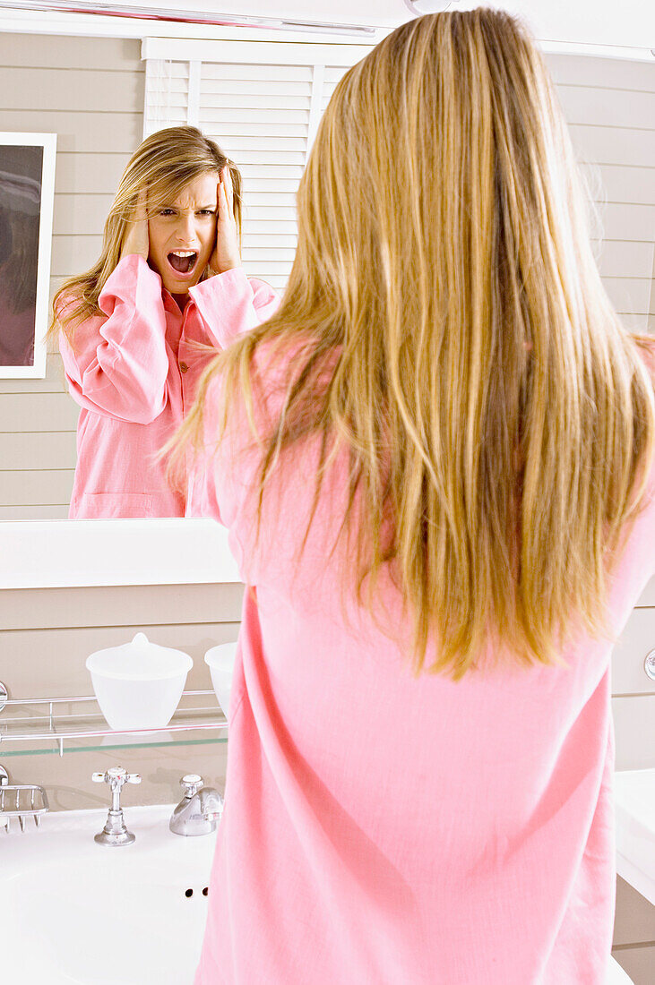 Reflection of a young woman looking in mirror and shouting