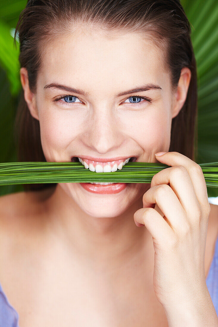 Young smiling woman holding plants between teeth