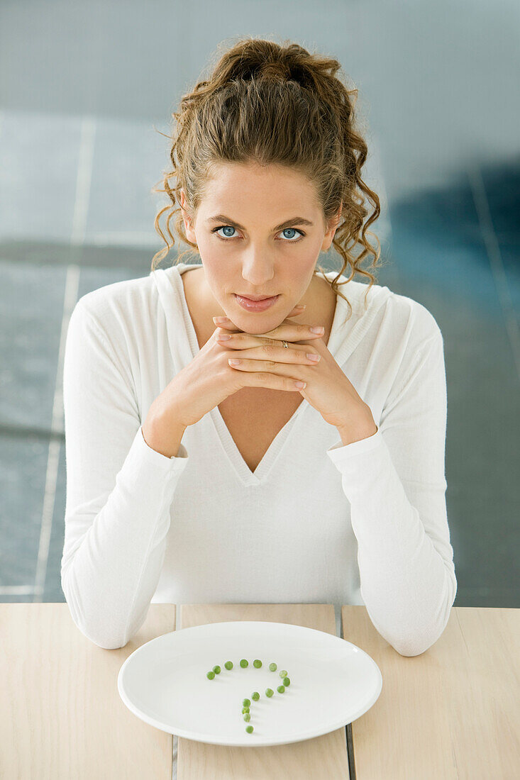 Frau sitzt an einem Tisch mit Erbsen in Fragezeichenform auf einem Teller