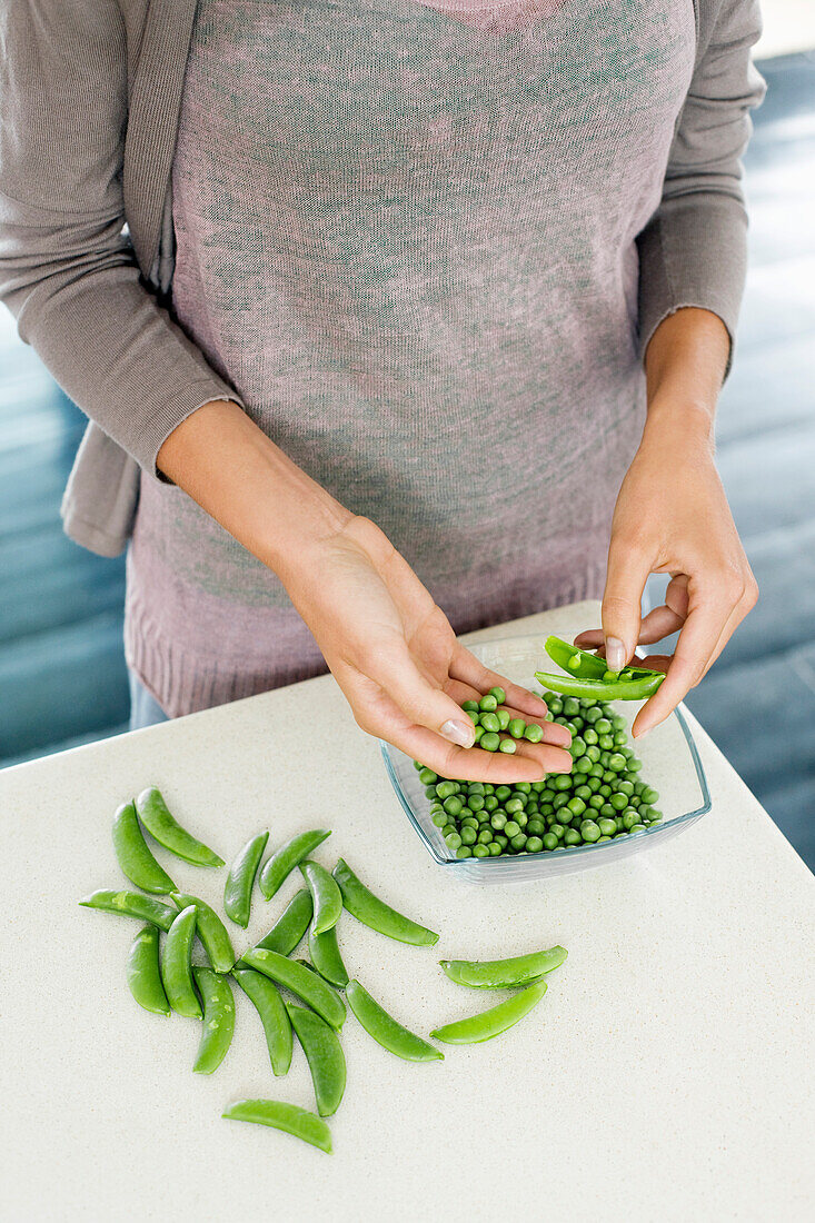 Woman peeling green peas in the kitchen