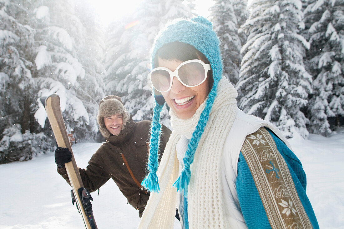 Young woman in winter clothes smiling at camera, man holding skis in background