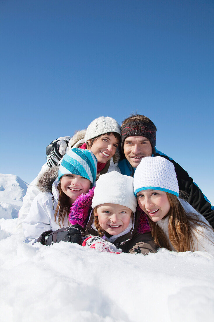 Happy family lying in snow, smiling at camera