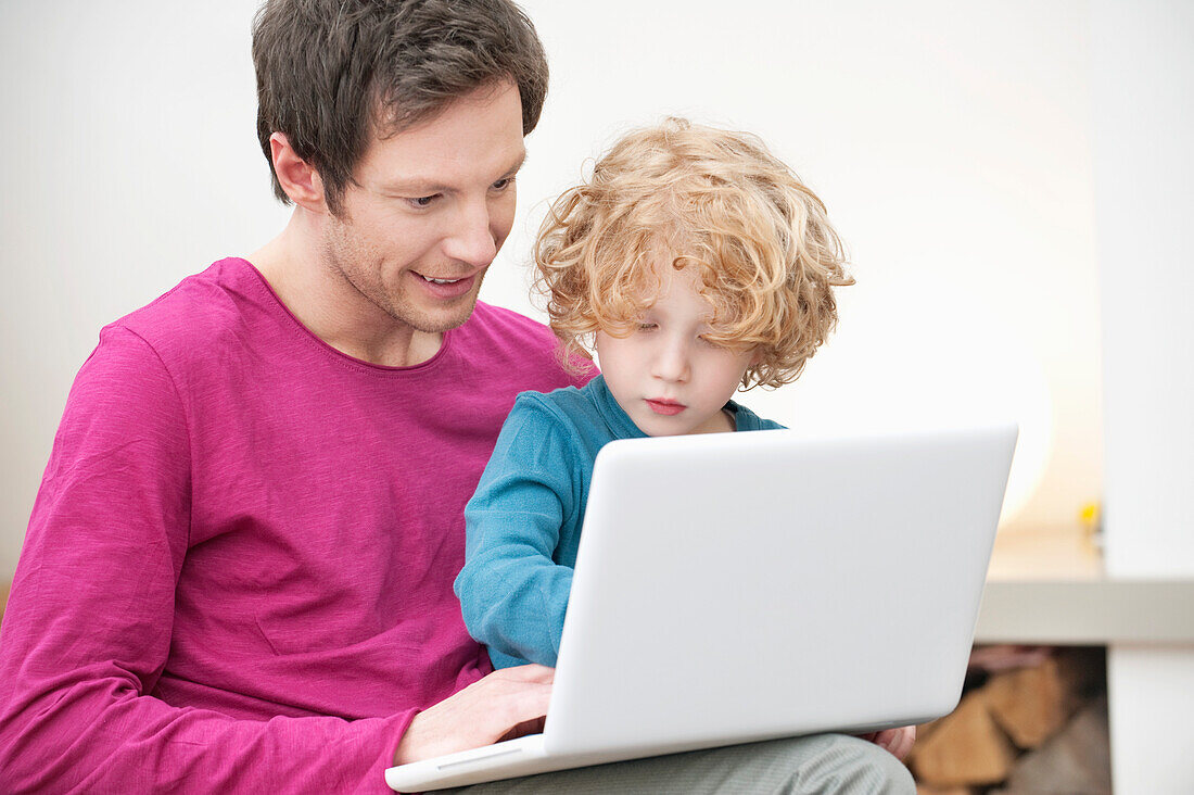 Close-up of a man assisting his son in using a laptop