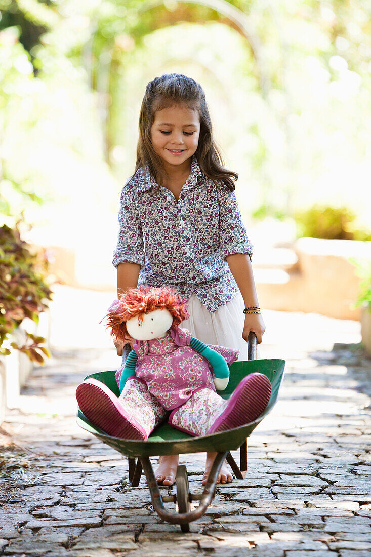 Cute girl pushing a wheelbarrow filled with toys