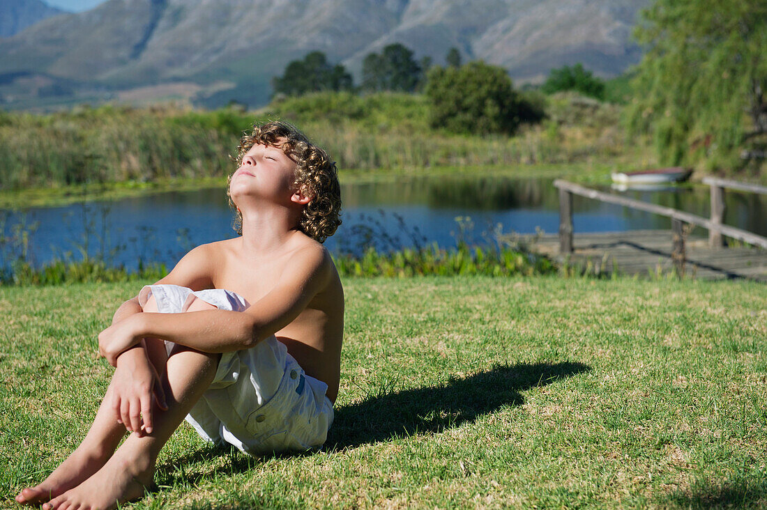 Shirtless little boy sitting with his eyes closed against mountain