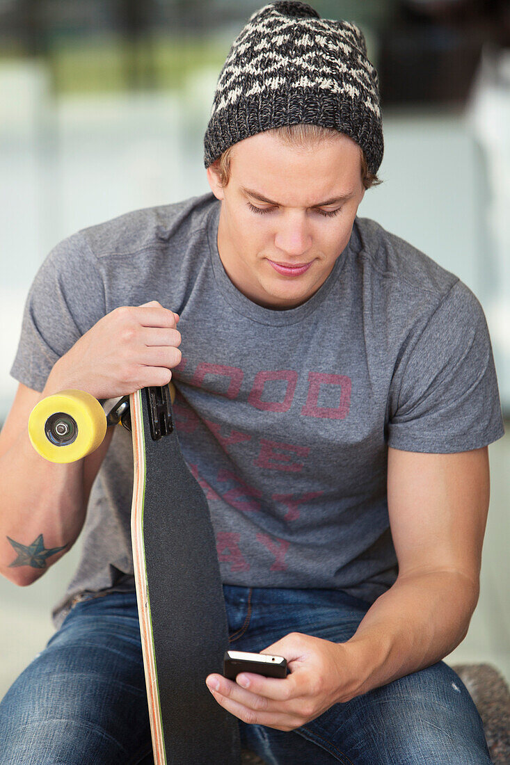 Young man holding skateboard and using a mobile phone