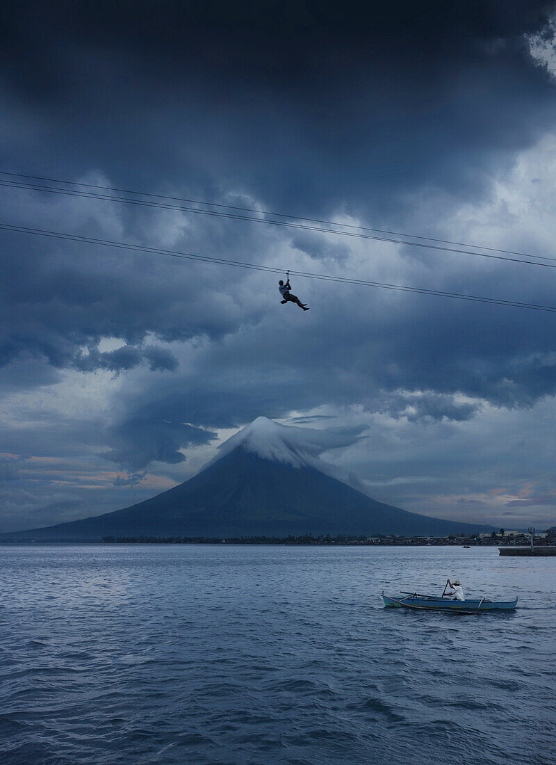 Mann an einer Seilrutsche und Fischer im Boot vor dem Vulkan Mayon, Legazpi Stadt, Luzon, Philippinen, Asien