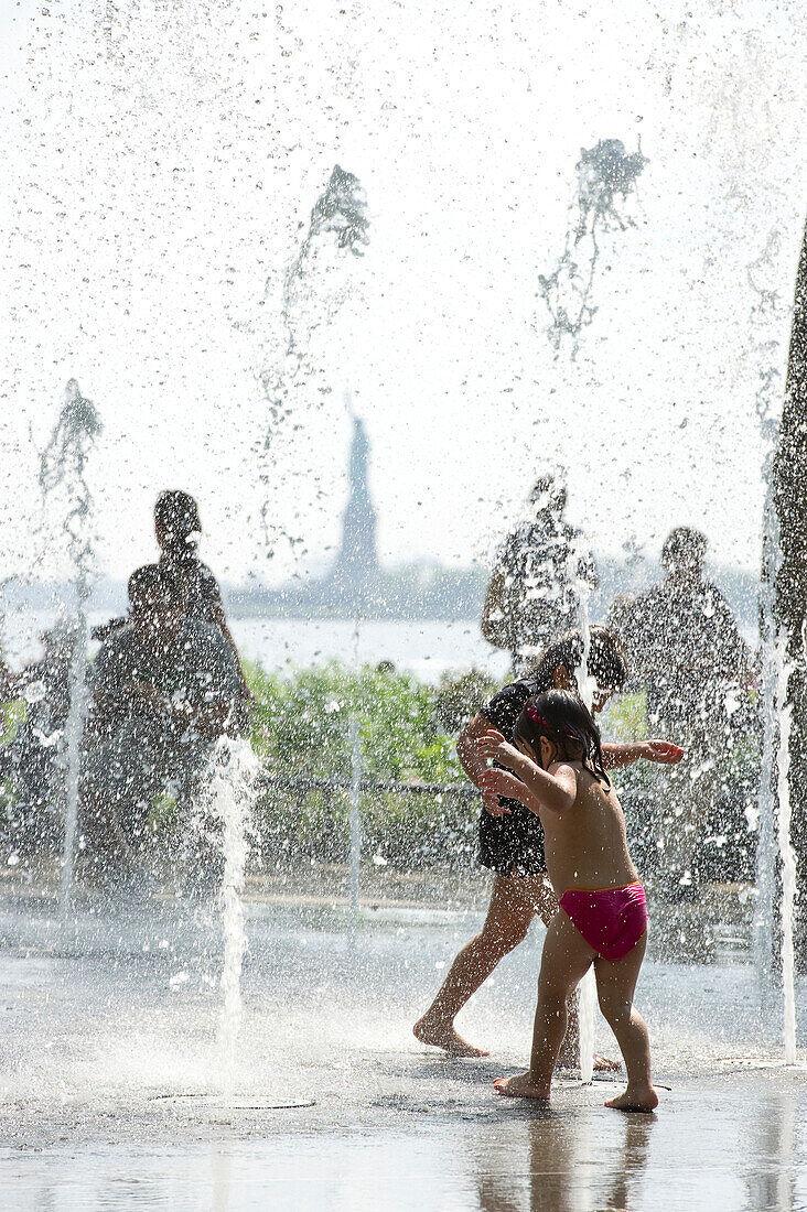 Kinder spielen zwischen Wasserfontänen im Battery Park, Freiheitsstatue im Hintergrund, Manhattan, New York City, New York, USA