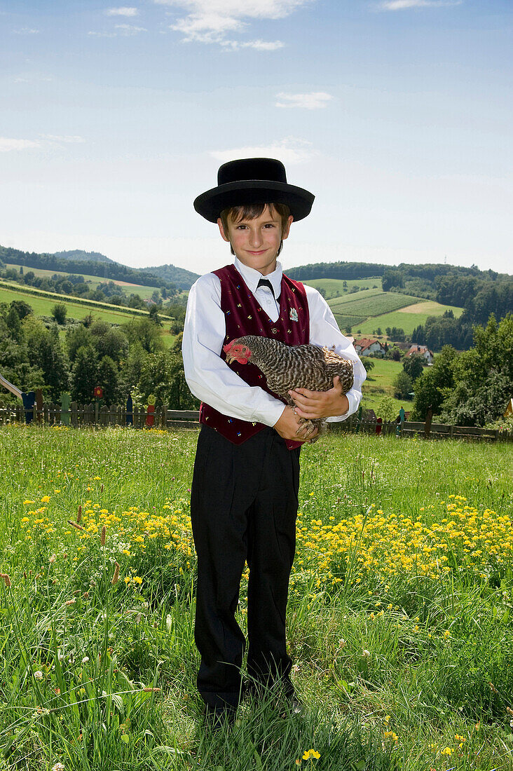 Boy holding a chicken wearing traditional Black Forest clothes, Gottertal, Baden-Wurttemberg, Germany