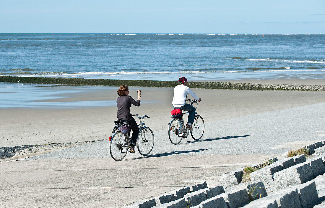 Two cyclists passing promenade, Norderney, East Frisian Islands, Lower Saxony, Germany