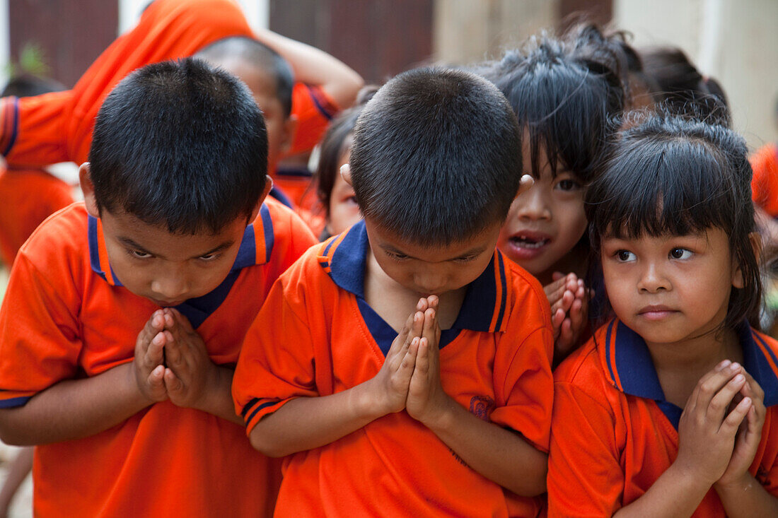 Junge Schulkinder in Uniform begrüßen Gäste mit traditioneller Wai Verbeugung, nahe Kanchanaburi, Thailand, Asien