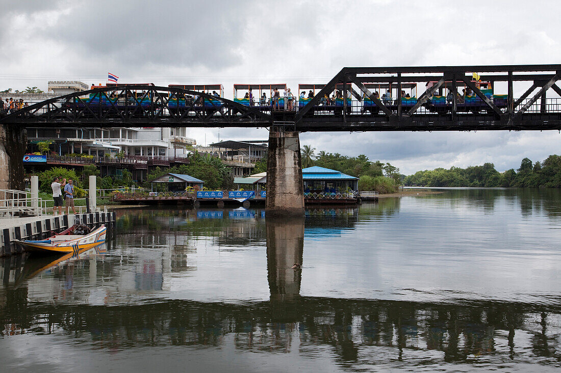 Eine Bimmelbahn fährt Touristen über die legendäre Brücke am River Kwai Fluss, Kanchanaburi, Thailand, Asien