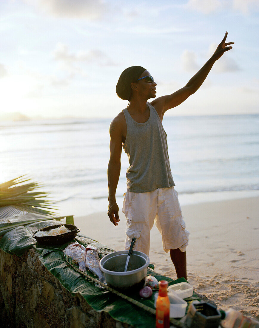 Mann bereitet Fisch auf kreolische Art zum Grillen vor, Strand von La Passe, im Hintergrund Nachbarinsel Praslin,  La Digue, La Digue and Inner Islands, Republik Seychellen, Indischer Ozean