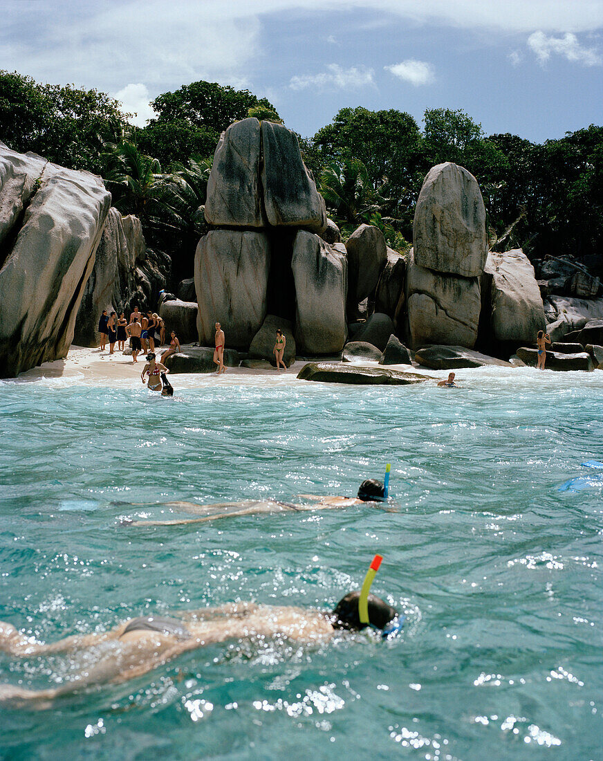 People snorkelling in shallow water over coral reef off tiny Coco Island, La Digue and Inner Islands, Republic of Seychelles, Indian Ocean