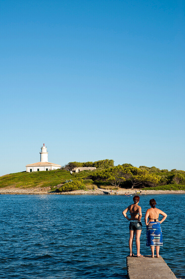 Girls enjoying the view of Alcanada Island and its lighthouse near Alcudia, Mallorca, Balearic Islands, Spain