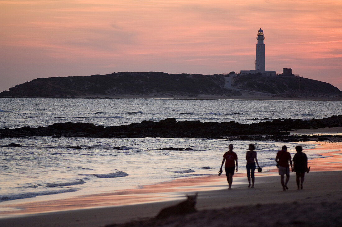 People walking on beach by lighthouse at sunset, Los Caños De Meca, Costa De La Luz, Spain