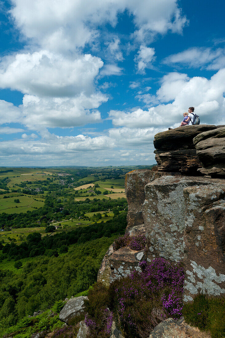 Mother and young girl sitting on rocks admiring view at Froggatt Edge across the Peak District, Froggatt, Derbyshire, England