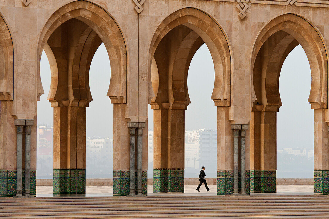 Woman walking past arches of the Hassan II mosque, Casablanca, Morocco