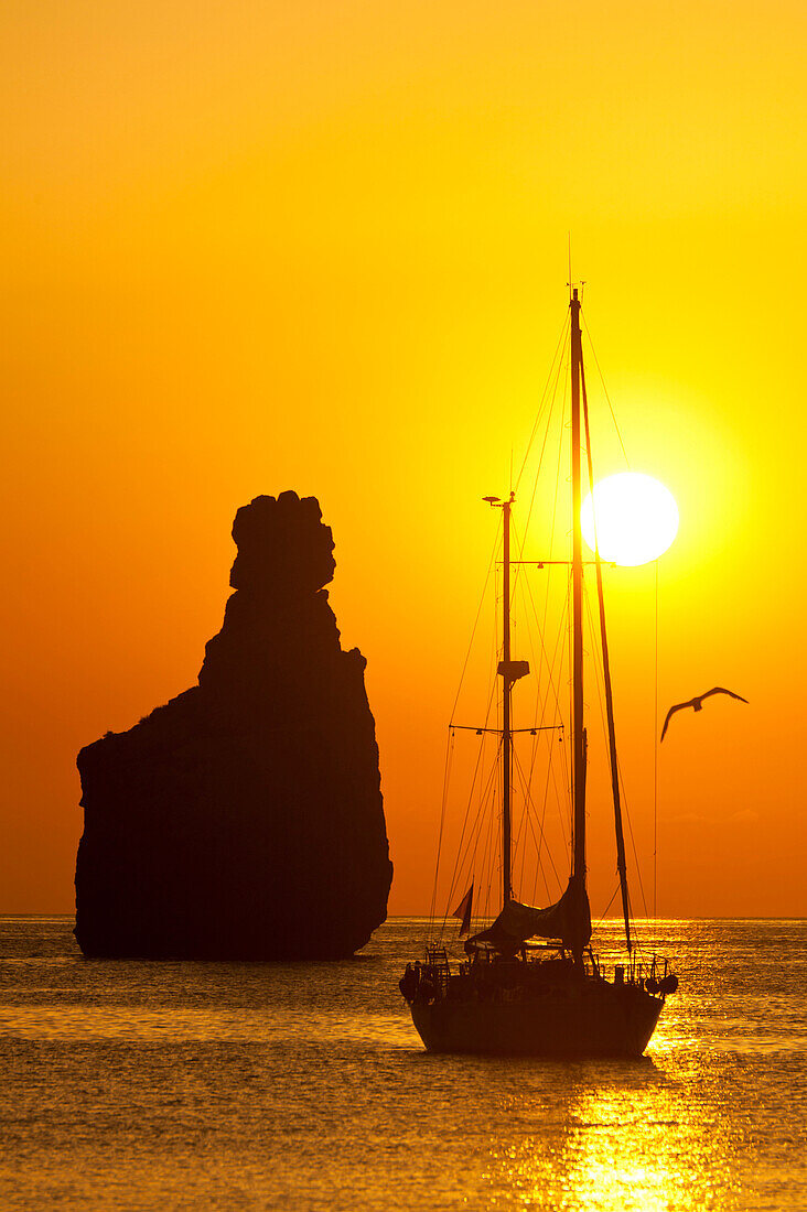 Yacht & strange shaped rock off Benirras beach at dusk, Ibiza, Spain