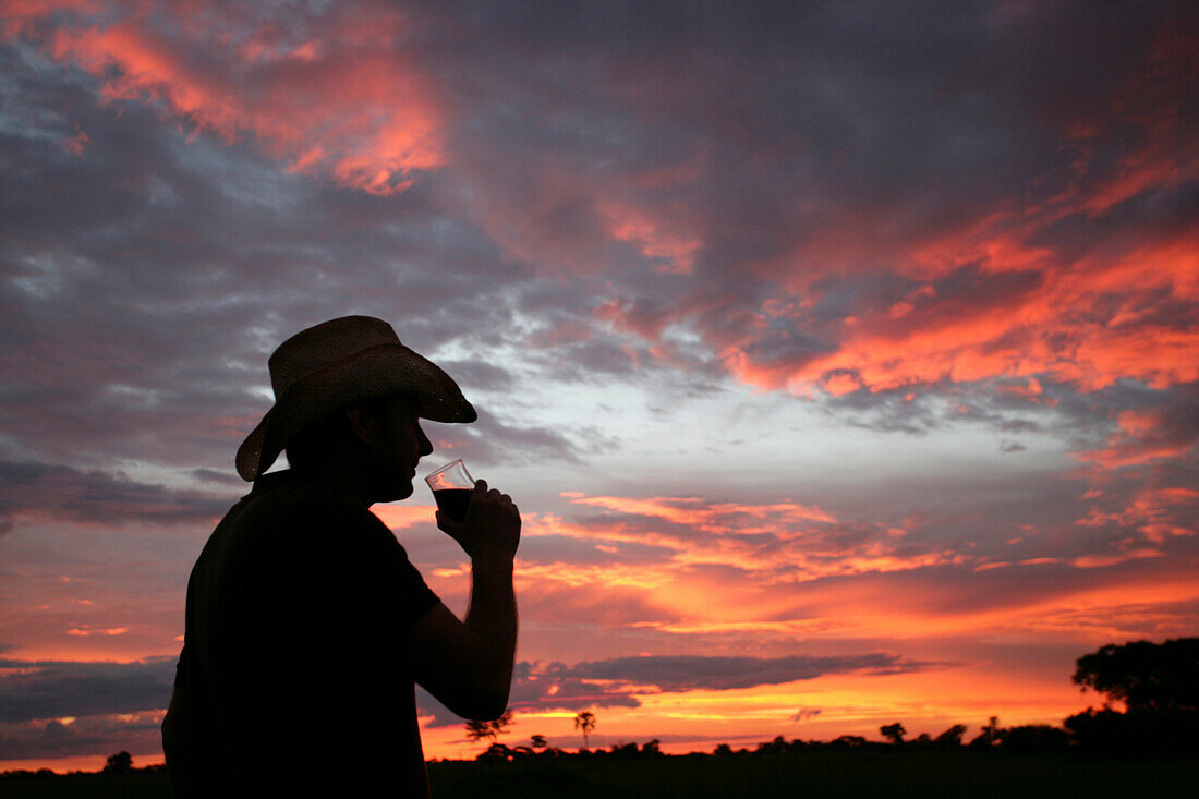 Man enjoying a drink at sunset, Okavango Delta, Botswana