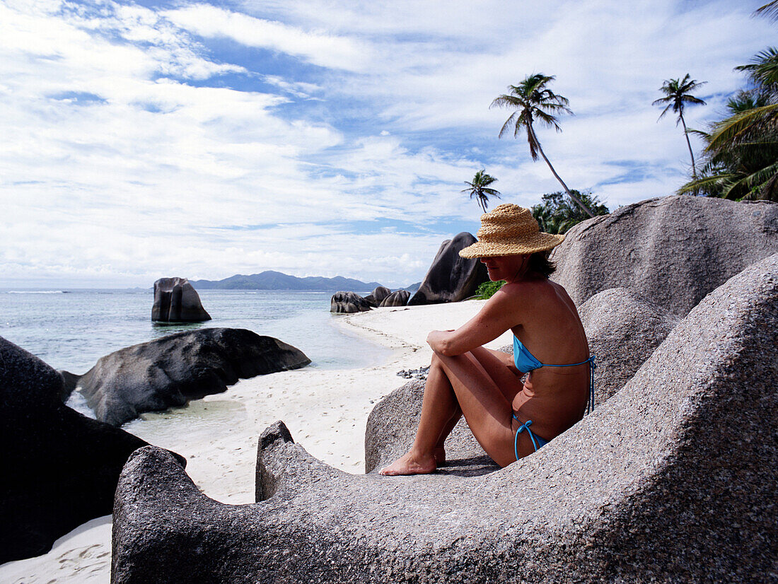 Woman sitting on rocks on the beach, Andse Source D'Argent, La Digue, Seychelles
