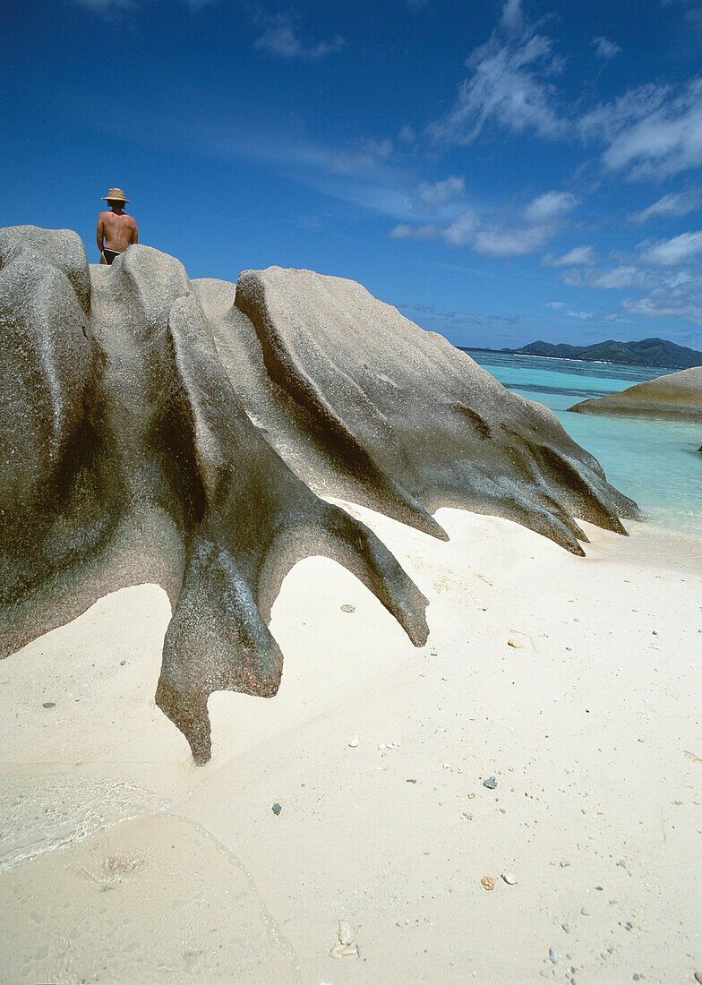 Woman sitting on a large rock on the beach, La Digue, Seychelles