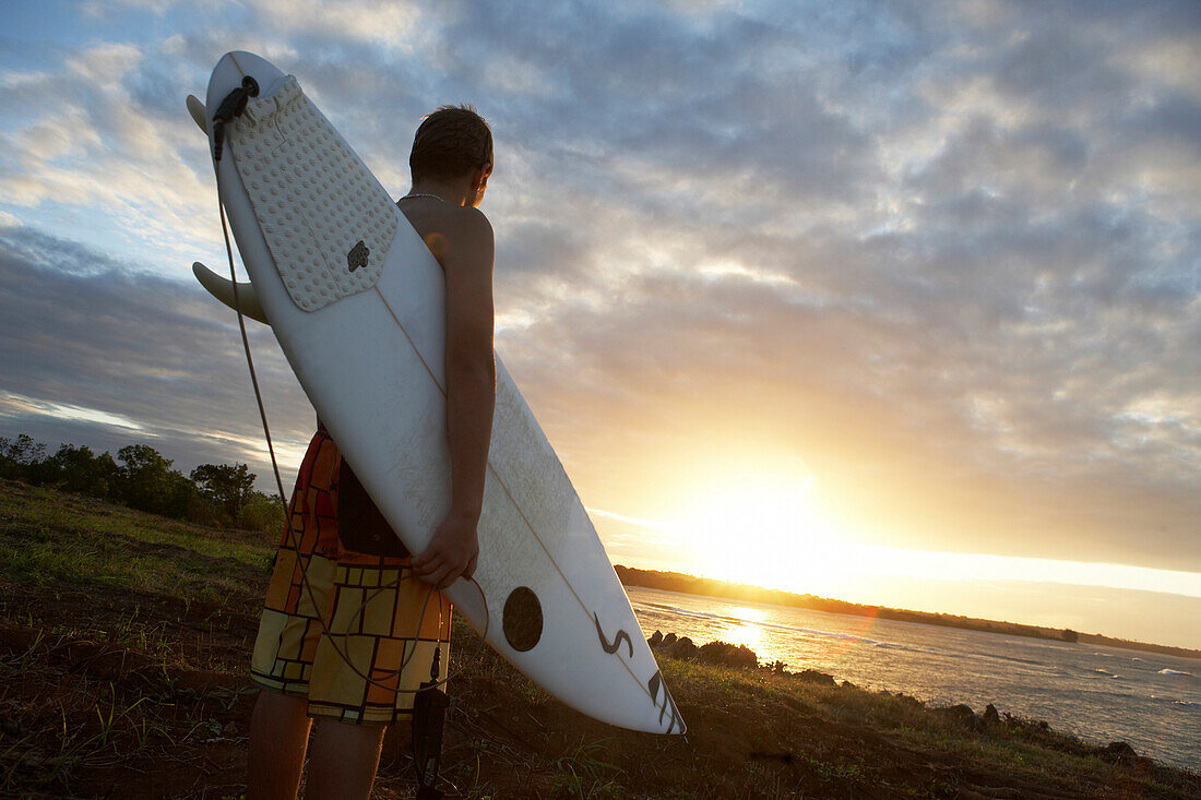 Man holding surfboard at sunset, Tanzania