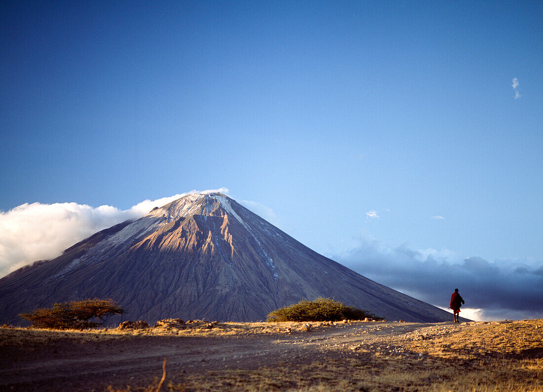Masaai man walking in front of Ol Donyo Lengai (East Africa's only active volcano), Tanzania, Africa