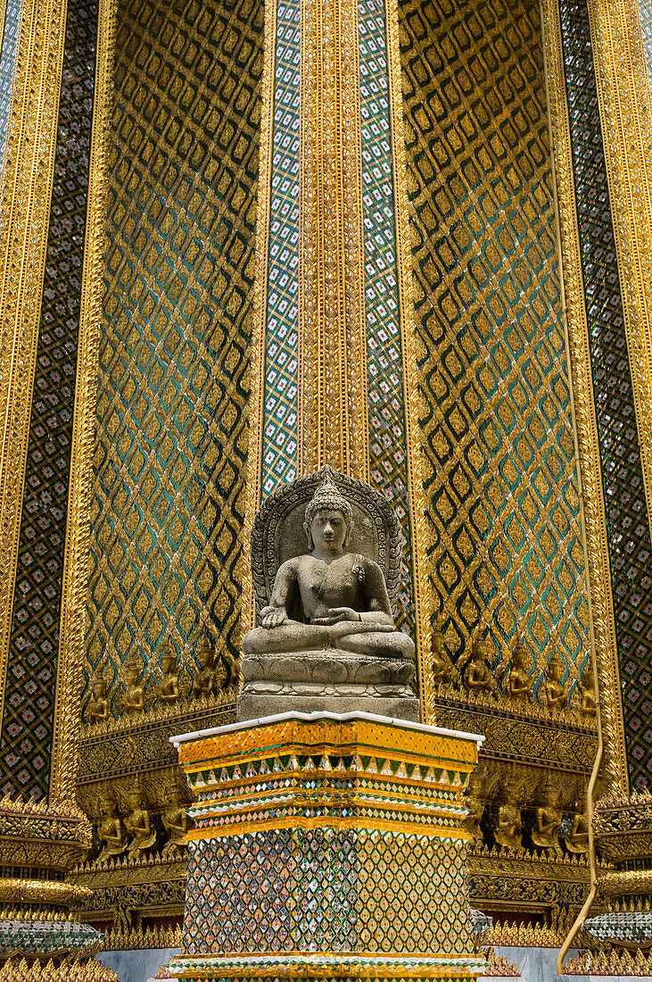 Small stone buddha statue beside columns of Wat Phra Kaew temple, Royal Palace complex, Bangkok, Thailand