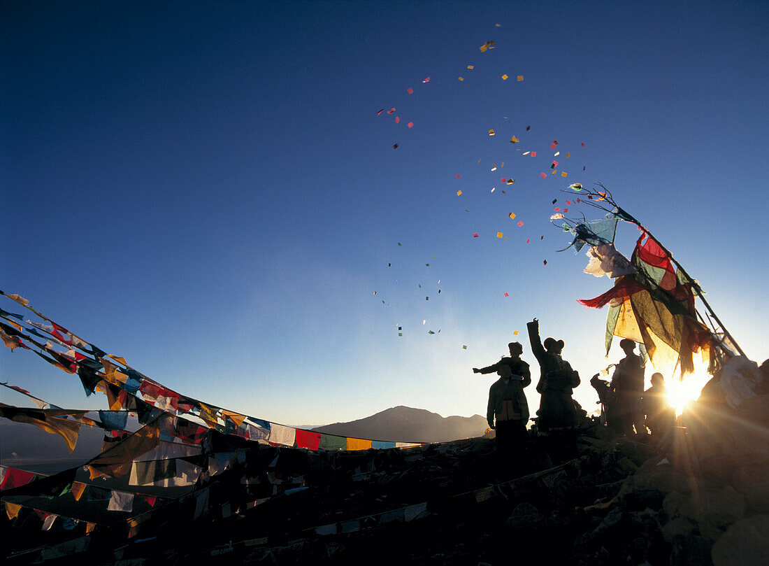 Pilgrims at dawn on hill beside prayer flags throwing windhorses into the air above Ganden Monastery for New Year, Tibet