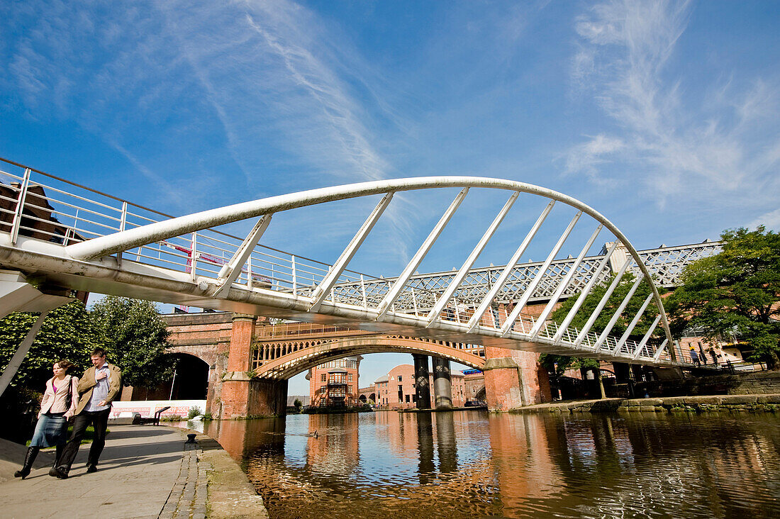 Couple walking under bridge by canal, Castlefield, Manchester, England