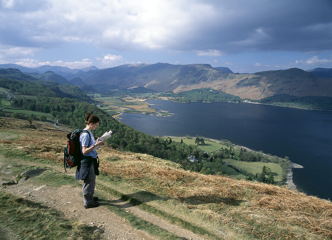 Walker reading map and looking past Derwent Water and up Borrow Dale as seen from Blueberry Fell, Lake District, England