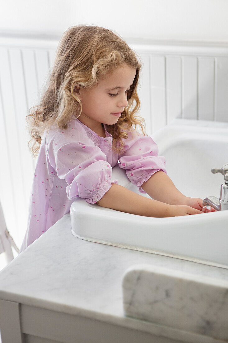 Cute little girl washing hands in bathroom sink