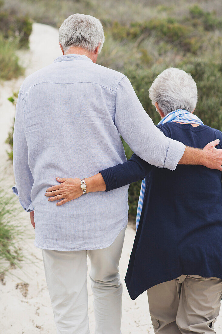 Rear view of a senior couple walking on the beach with their arms around each other