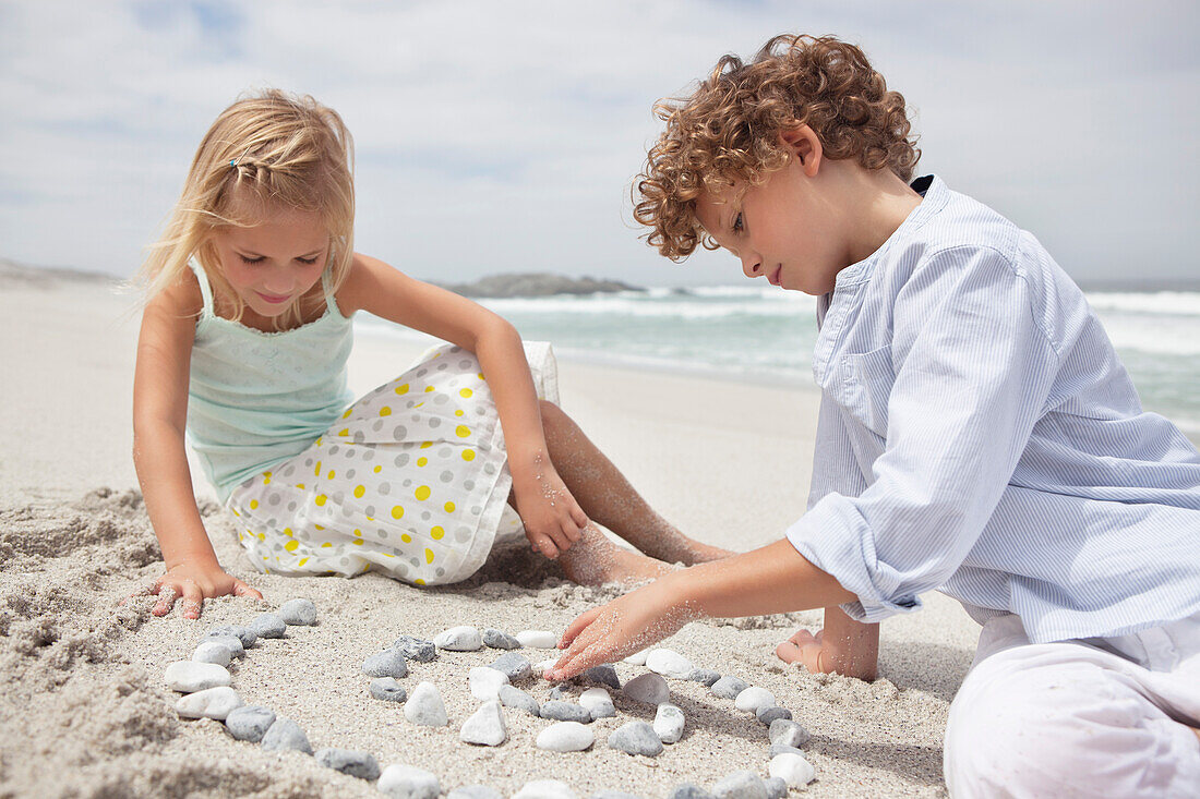 Siblings playing with pebbles on beach