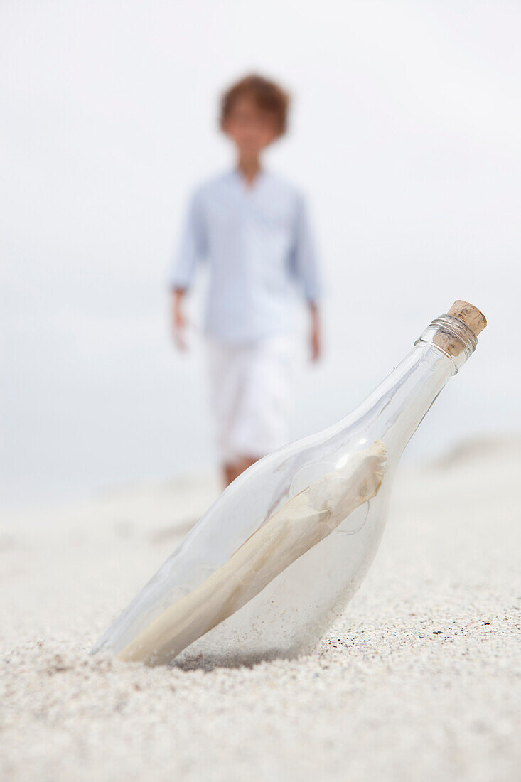 Blurred boy walking towards bottle with note inside on beach