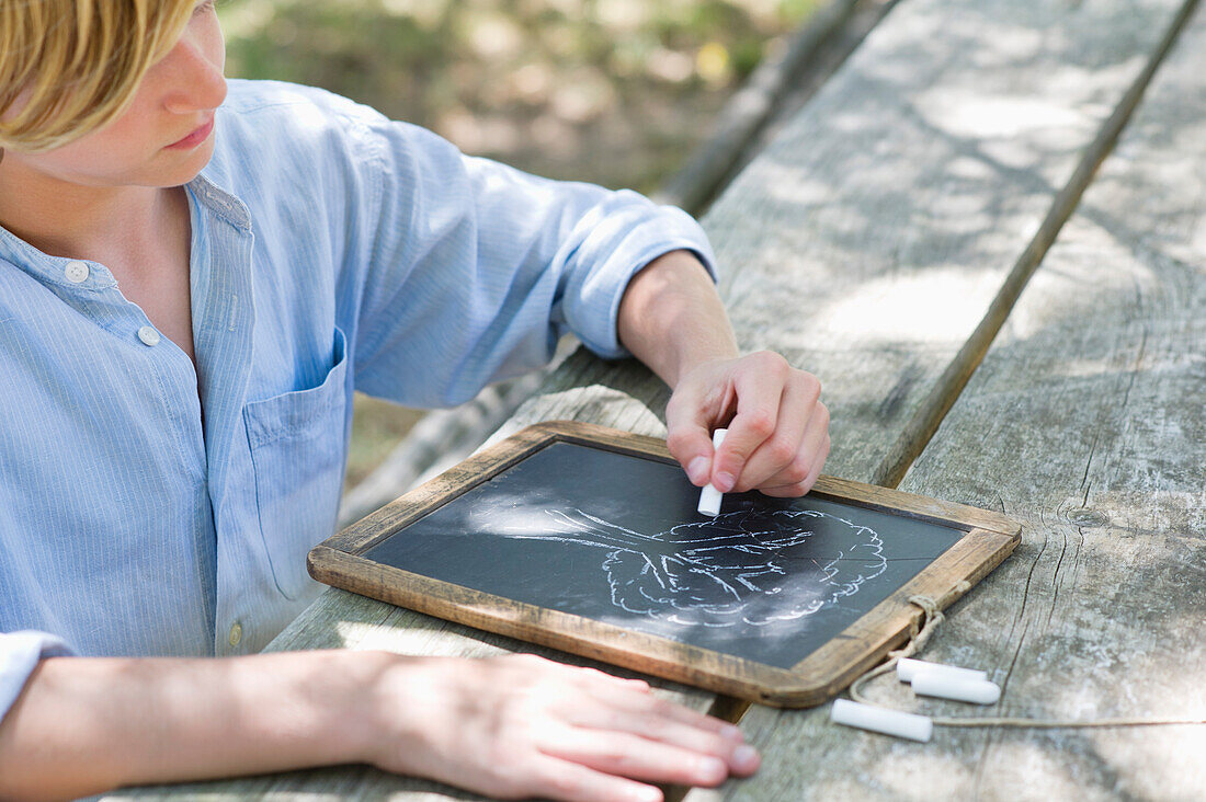 Side profile of a little boy making drawing of tree on slate outdoors