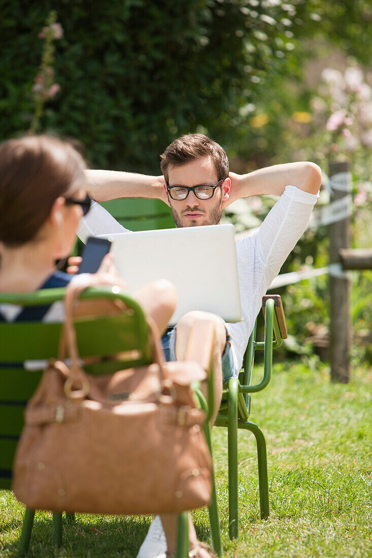 Man sitting in a garden and looking at a laptop, Paris, Ile-de-France, France