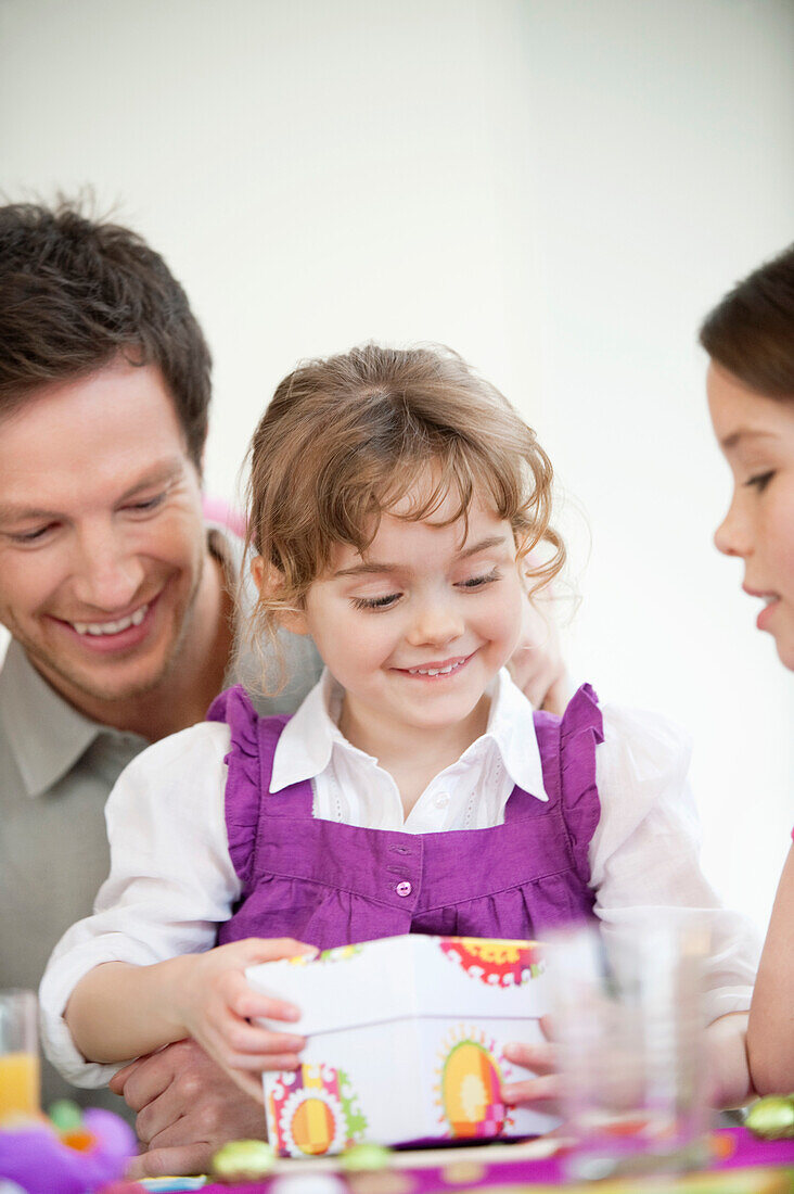 Girl opening her birthday present with her father and sister