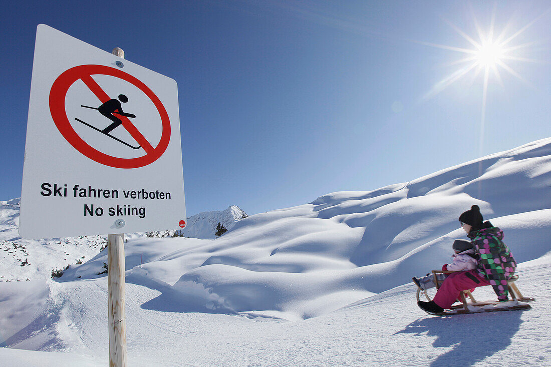 Geschwisterkinder, 12 und 2 Jahre, auf Rodelschlitten, Verbotsschild, Klösterle, Arlberggebiet, Österreich