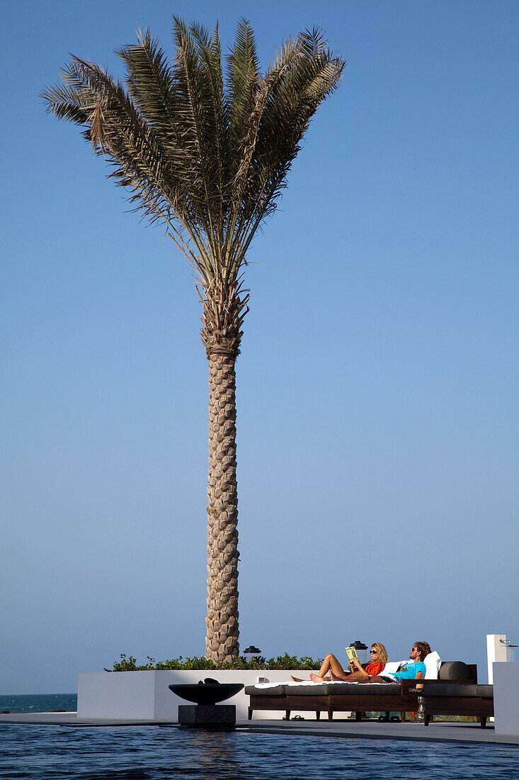 Junges Paar entspannt sich auf Liegestühlen, The Long Pool Schwimmbad, The Chedi Muscat Hotel, Muscat, Maskat, Oman, Arabische Halbinsel